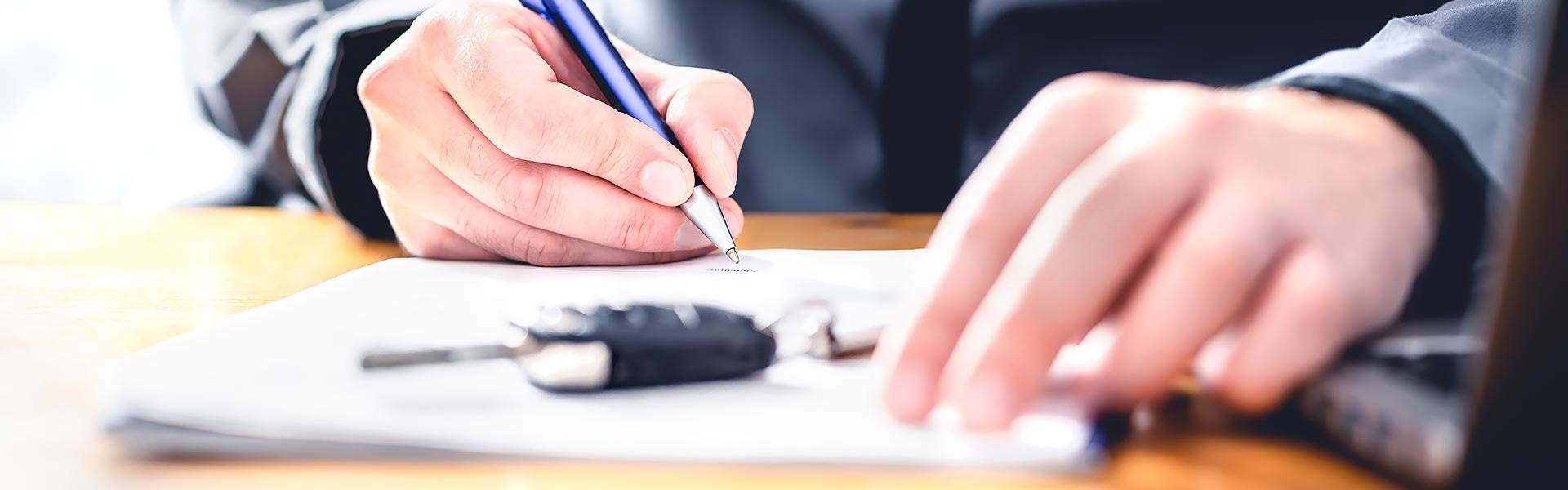 Close up of a man signing a form with new car keys sitting on top of it.